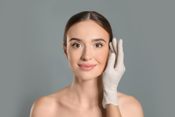 Wall Mural - Doctor examining woman's face before plastic surgery on grey background