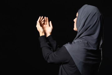 Wall Mural - Beautiful Muslim woman praying against dark background