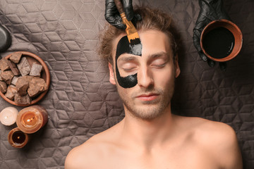 Wall Mural - Cosmetologist applying mask onto man's face in spa salon