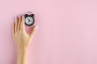 © Sviatoslav Kovtun - Hand with analog alarm clock composition on pink background.