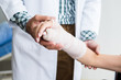 © Thinapob - Close-up of man doctor of checking splint the arm of female patient hand due to with her arm broken for better healing with a smile sit in a wheelchair In the room hospital background.