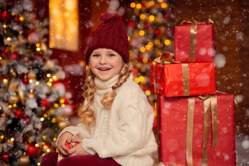 Wall Mural - happy cheerful girl in a hat and with pigtails on the veranda of the house in anticipation of Christmas