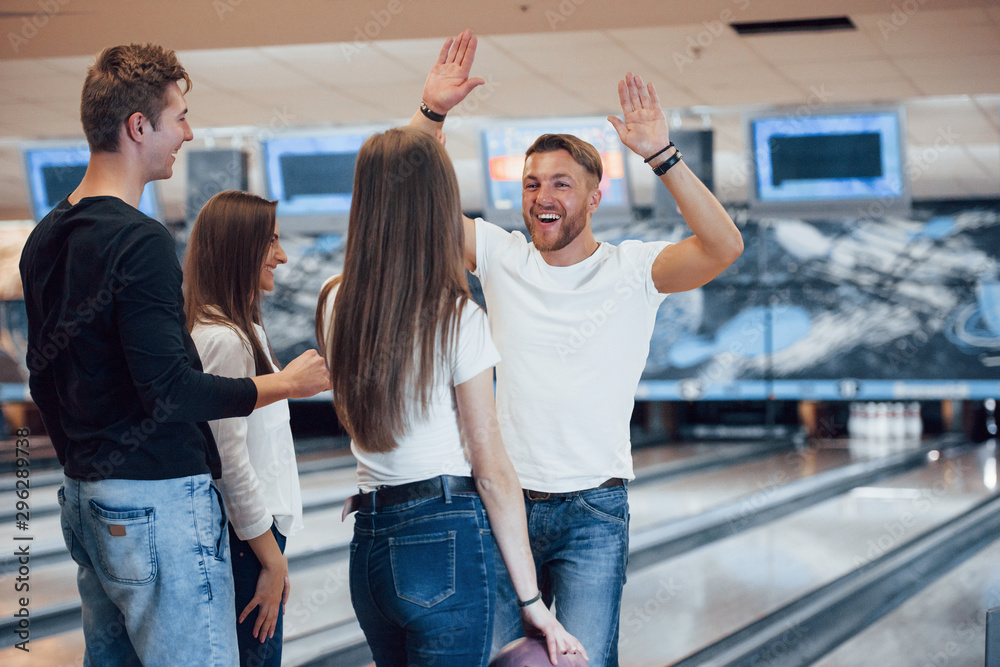 I want your high five. Young cheerful friends have fun in bowling club ...