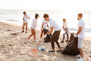 Wall Mural - Image of young voluntary workers cleaning beach from plastic at seashore