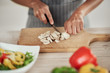 © nenadaksic - Close up of mixed race woman in apron standing in kitchen and chopping mushrooms.