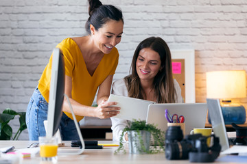 Wall Mural - Two young businesswomen talking and reviewing they last work in the digital tablet in the office.