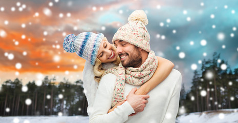 Poster - couple, christmas and holidays concept - smiling man and woman in hats and scarf hugging over winter forest background