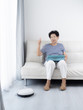 © nuiiko - Senior woman unsing tablet while robot vacuum cleaning floor at home. Modern lifestyle concept.