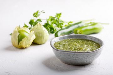 Tomatillo salsa verde. Bowl of spicy green sauce on white table, mexican cuisine.