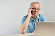 © amixstudio - Elderly Caucasian man in glasses with a serious expression on his face working on a laptop at his desk on a white background