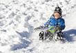 Cute young boy sprayed with snow as he is sledging down a hill