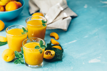 Wall Mural - Glass of fresh healthy apricot or peach smoothie or juice on light blue concrete surface table. Sunny light. Shallow depth of the field, close up, copy space for you text