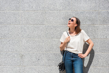 Wall Mural -  cheerful older woman laughing by wall with handbag and sunglasses