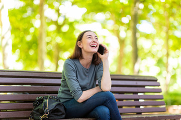 Wall Mural - happy woman sitting on park bench talking with cellphone