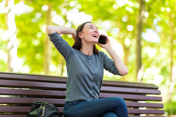 Wall Mural - cheerful woman sitting on park bench talking with cellphone