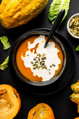 Wall Mural - Pumpkin cream soup with milk and pumpkin seeds in a black bowl on the black background. Close-up.