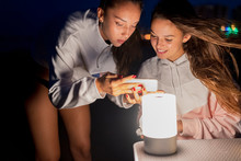 Two Female, Friends With Smartphone And Led Light On Camping Table At Night