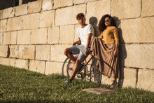 Young Couple With Bicycle, Leaning On Stone Wall, Looking Cool