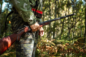 A hunter with a gun in his hands in hunting clothes in the autumn forest close-up. The hunting period, the fall season is open, the search for prey.