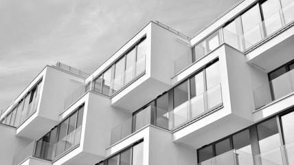  Fragment of a facade of a building with windows and balconies. Modern home with many flats. Black and white.