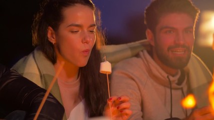 Poster - leisure and people concept - group of smiling friends roasting and eating marshmallow at night camp fire