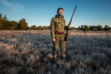 Hunter Man In Camouflage With A Gun During The Hunt In Search Of Wild Birds Or Game On The Background Of The Autumn Forest. Autumn Hunting Season. The Concept Of A Hobby, Killing.