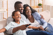 © Prostock-studio - African American Family Of Three Sitting On Sofa Watching Television