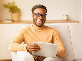 Poster - Happy Guy Using Digital Tablet Sitting On Sofa Indoor