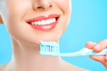 Wall Mural - Young beautiful woman is engaged in cleaning teeth. Beautiful smile healthy white teeth. A girl holds a toothbrush. The concept of oral hygiene. Promotional image for a stomatology, dental clinic.