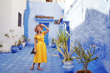 Wall Mural - Colorful traveling by Morocco. Young woman in yellow dress walking in  medina of  blue city Chefchaouen.