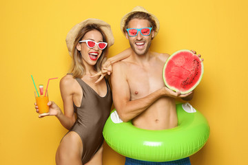 Poster - Happy young couple in beachwear with inflatable ring and cocktail on color background