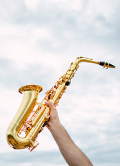 Hand Holding saxophone with cloudy and soft sky background. Music concept with copy space top.