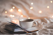 © morrowlight - Cup of coffee staying on open book over lights at background at night closeup.