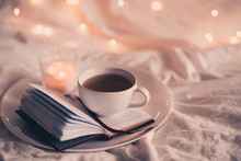 Cup Of Coffee With Open Book In Bed Over Lights Closeup. Good Night.