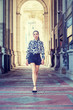 © Alexander Image - Young American Woman Street Fashion in New York City. South American College Student with ponytail hairstyle, wearing long sleeve patterned shirt, black short skirt, walking on narrow vintage street..