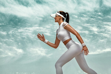 Wall Mural - Sporty young woman and fit athlete runner running on the sky background. The concept of a healthy lifestyle and sport. Woman in white sportswear.