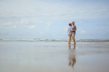 Wall Mural - Senior couples embrace on the beach at sunny day, plan life insurance with the concept of happy retirement.