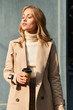 © Anton - Beautiful sunny blond girl in coat with coffee to go dreamily standing outdoor