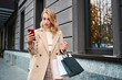 © Anton - Beautiful stylish blond girl in beige coat with shopping bags using cellphone on city street