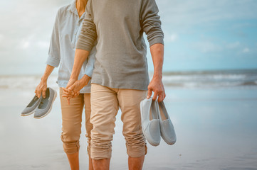 Senior couples walking carrying shoes on the beach at sunny day, plan life insurance with the concept of happy retirement.