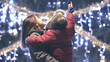 © MEDIAIMAG - Portrait of mother holding child in her arms and admiring Christmas tree outdoor