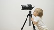 © MEDIAIMAG - Funny baby child looking on photo camera scree on tripod, determined to work