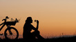 © MEDIAIMAG - Isolated young woman silhouette sit close bike on hill, copy space