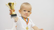 © MEDIAIMAG - Portrait of baby child rising up golden cup, kid offering his victory trophy