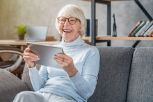 Senior Woman Looking And Laughing At Her Digital Tablet On Sofa