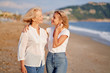 © luengo_ua - Outdoor portrait of smiling happy caucasian senior mother with her adult daughter hugging and walking on sea beach.