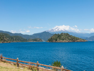 The amazing Choshuenco Volcano surrounded by clouds, over the waters of Lake Panguipulli, in southern Chile.