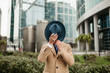 © Marat - A businessman in a beige coat stands in the business district and covers his face with his hat