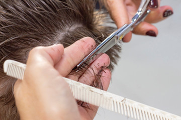 The hands of young barber making haircut to attractive man in barbershop. mens hair cutting scissors in a beauty salon