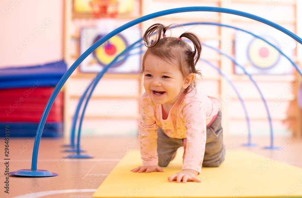 Baby toddler crawling on floor through tonnel in gym class. Lifestyle concept of children active games and exercises. - obrazy, fototapety, plakaty 
